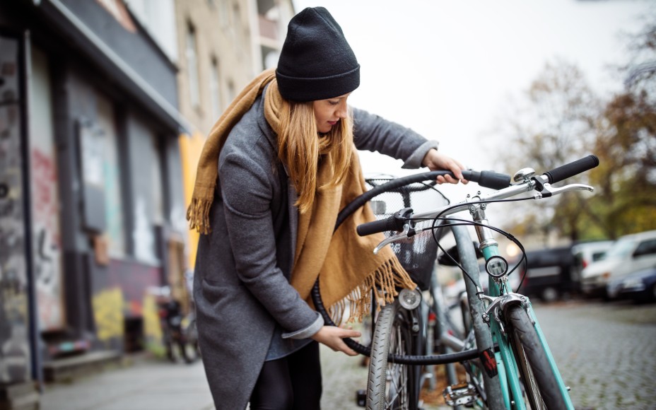 Frau mit langen blonoden Haaren, Mütze und Schal schließt ihr Fahrrad ab