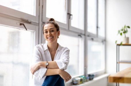 Eine lächelnde Frau sitzt in einem modernen Loftraum auf der Fensterbank