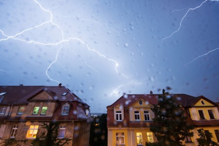 Zwei Stadtvillen bei Nacht während am Himmel mehrere Blitze zucken