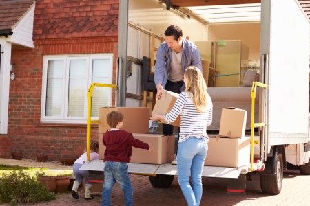 Junge Familie mit zwei Kindern zieht in ein geklinkertes Reihenhaus und trägt Kartons die Treppe rein.