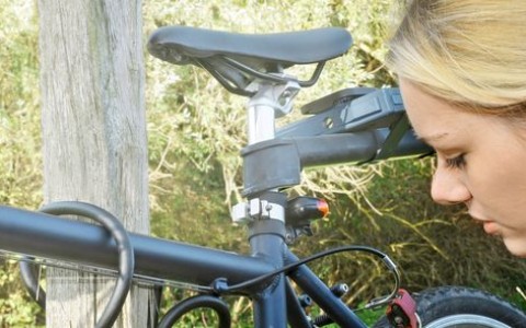 Blonde Frau mit Zopf und großen Perlohrringen kniet neben ihrem Mountainbike und inspiziert etwas.