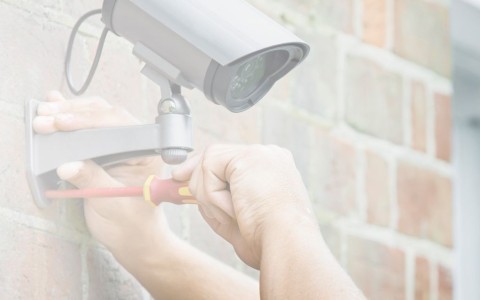 Mann schraubt eine Überwachungskamera an einer Hauswand an