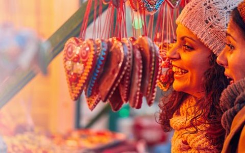Zwei Freundinnen mit Mützen stehen an einem Weihnachgtsmarktstand mit vielen Lebkuchenherzen