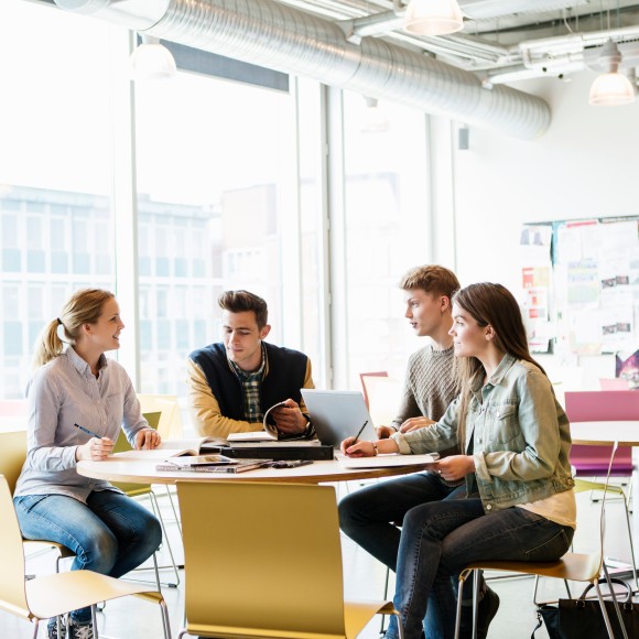 Studenten diskutieren an einem runden Tisch, Laptops stehen auf dem Tisch