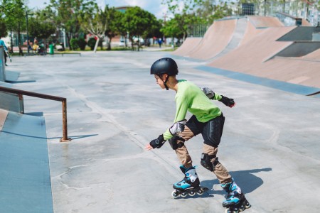 Junge in kompletter Schutzausrüstung skatet mit Inlinern in einer Halfpipe