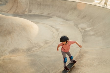 Kleiner Junge mit Helm fährt in einer Halfpipe Skateboard