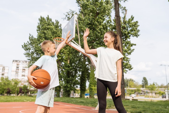 Ein Teenagermödchen und eine kleiner junge geben sich High Five, während der Junge einen Basketball unter den rechten Arm klemmt