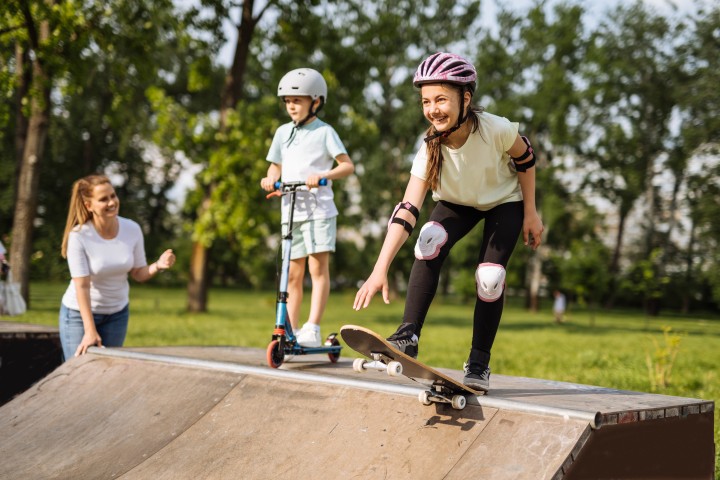 Kinder unterschiedlichen Alters sind mit Helmen, Skateboards und Rollern in einer Halfpipe