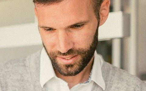 Mann in grauem Pullover steht in einem Büro und schaut etws auf einem Tablet