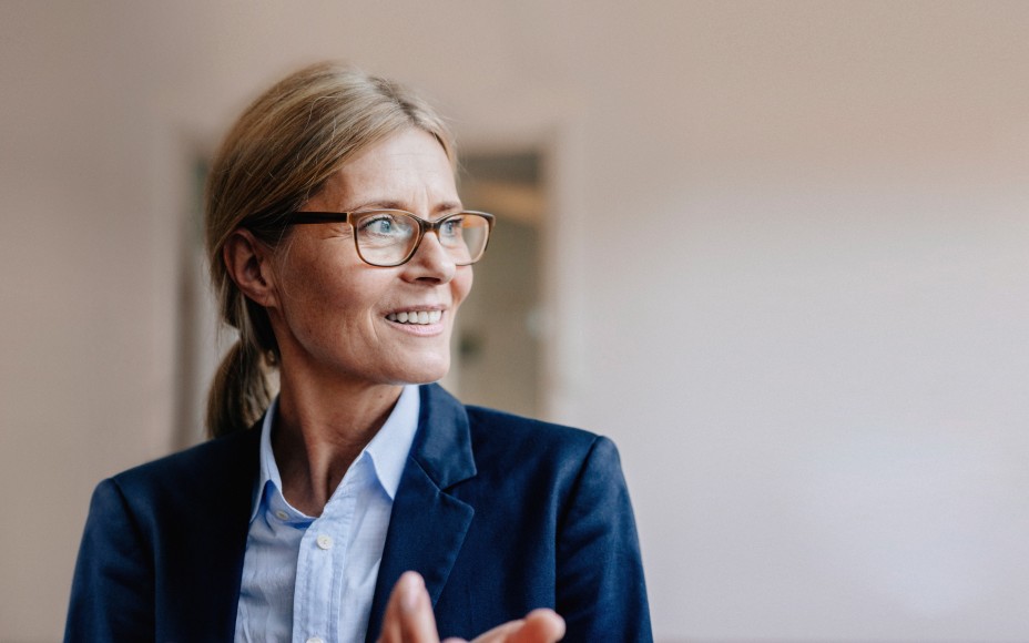 Blonde Businessfrau mit Zopf und Brille im Hosenanzug schaut lächelnd nach links