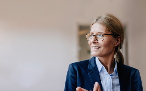 Blonde Businessfrau mit Zopf und Brille im Hosenanzug schaut lächelnd nach links