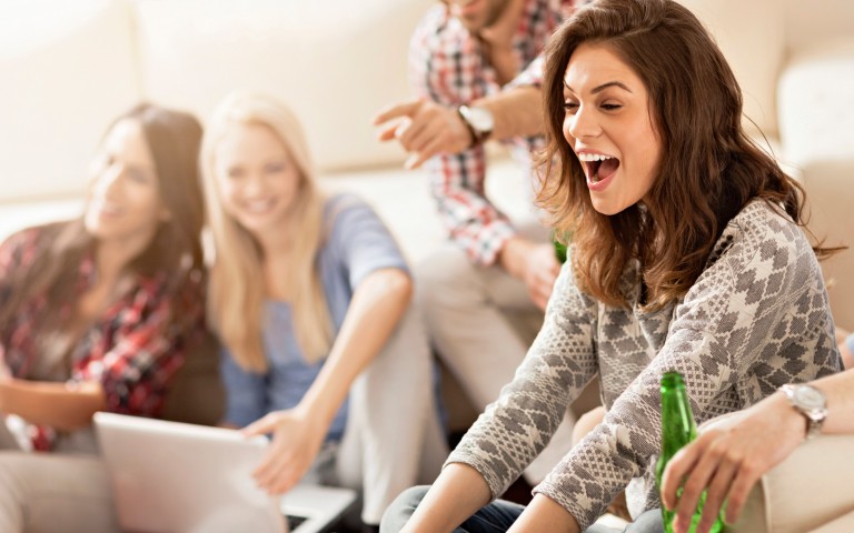 Junge Leute lachen zusammen und sitzen in einem Wohnzimmer auf Sofas