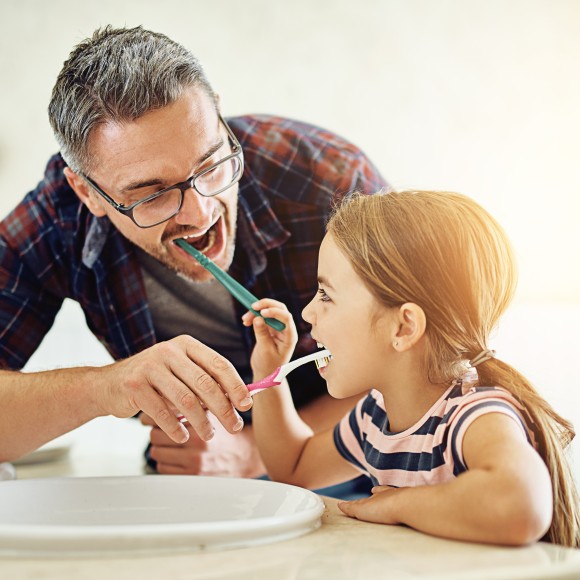 Ein Mann und seine kleine Tochter putzen zusammen die Zähne