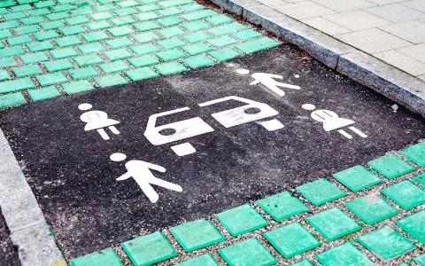 Grüne Pflastersteine und Strichmännchen auf schwarzem Asphalt markieren einen Carsharing-Platz
