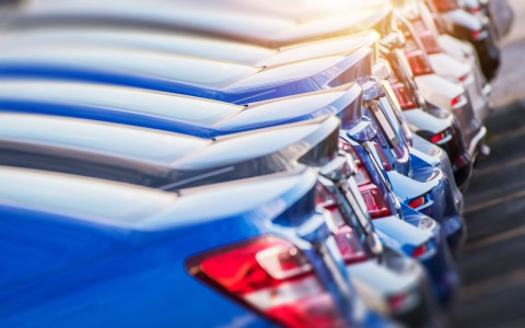 Eine Reihe verschiedenfarbiger Limosinen mit Stufenheck steht nebeneinander in der Abendsonne, die sich in den Autos spiegelt