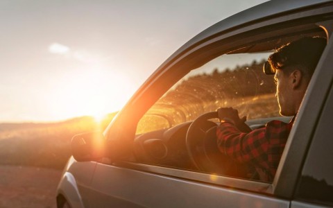 Junger Mann im karierten Hemd fährt in der untergehenden Sonne auf einer Landstraße