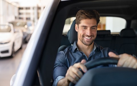 Männlicher Fahrer in einem weißen Auto sitzt am Steuer, das sich auf der rechten Seite befindet