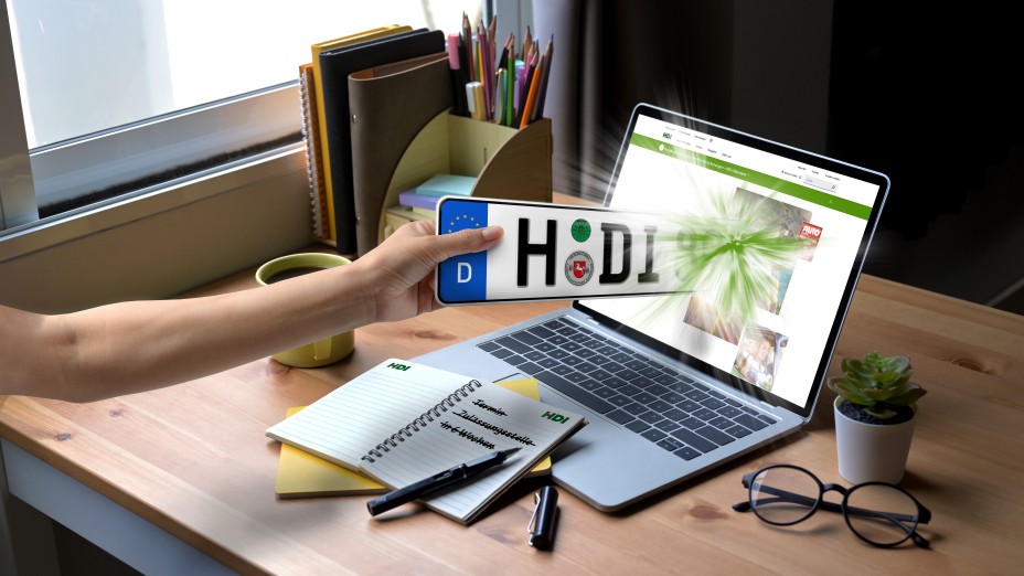 Männliche Hand hält ein Kennzeichen mit H-DI in die Kamera, im Hintergrund ein Laptop, auf dem die Kfz-Versicherungsseite von HDI zu sehen ist