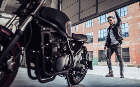 Mann mit Sonnenbrille öffnet ein Garagentor nach oben, u in der Garage an sein Motorrad zu gelangen