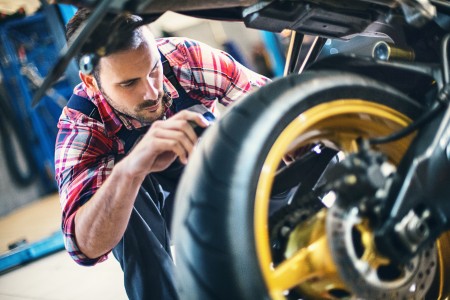 Mann in kariertem Hemd und Latzhose inspiziert den Hinterreifen eines Motorrads