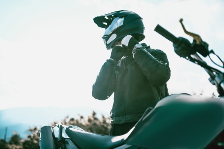 Männlicher Motorradfahrer steht neben seiem Bike und schließt gerade den Gurt seines Motorradhelms