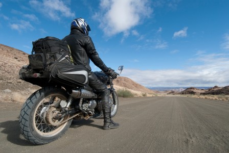 Voll beladenes Motorrad von hinten gesehen fährt bei strahlendem Sonnenschein durch eine karge Gebirgslandschaft