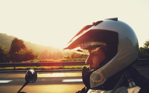 Seitenansicht eines männlichen Motorradfahrers mit silbernem Helm in der Abendsonne auf der Straße