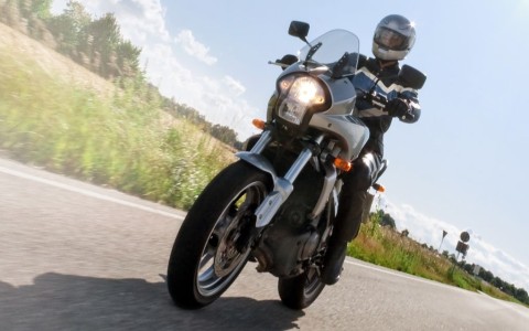 Biker in Schutzkleidung auf einer silbernen Tourer-Maschine fährt auf einer Landstraße, Felder rechts und links, die Sonne scheint