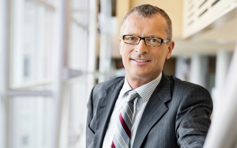 Eingrauhaariger Manager mit Brille im grauen Nadelstreifenanzug und Krawatte lächelt in die Kamera