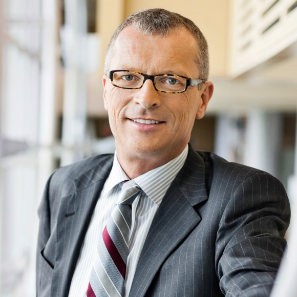Eingrauhaariger Manager mit Brille im grauen Nadelstreifenanzug und Krawatte lächelt in die Kamera