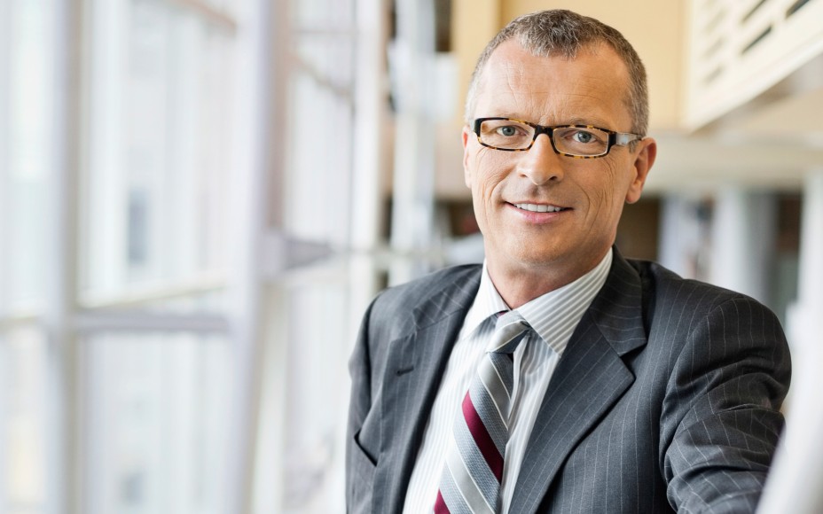 Eingrauhaariger Manager mit Brille im grauen Nadelstreifenanzug und Krawatte lächelt in die Kamera