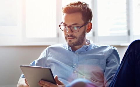 Mann mit Brille sitzt entspannt und nutzt ein Tablet bei Tageslicht