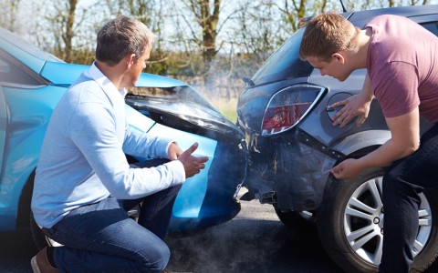 Zwei Männer begutachten einen Auffahrunfall zwischen zwei Autos mit sichtbarem Schaden und Rauch