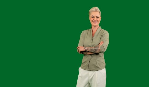 Doc Caro steht mit verschränkten Armen in sportlicher Kleidung vor grünem Hintergrund