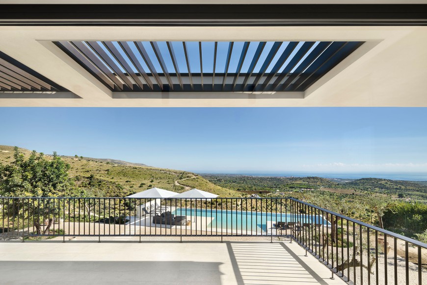 Blick von einer überdachten Terrasse mit Blick auf einen modernen Pool, im Hintergrund grüne Hügel und das Meer