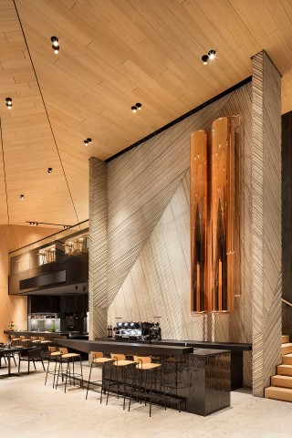 Moderne Halle mit Böden, Wänden und Decke aus hellem Holz, schwarzen Elemente mit einer Bar und einer glänzenden Skulptur an der Wand