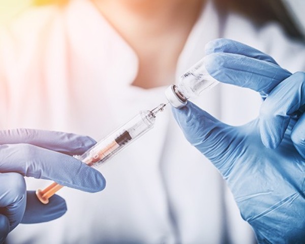 Ärztin mit blauen Handschuhen zieht eine Spirtze mit einem Medikament auf.