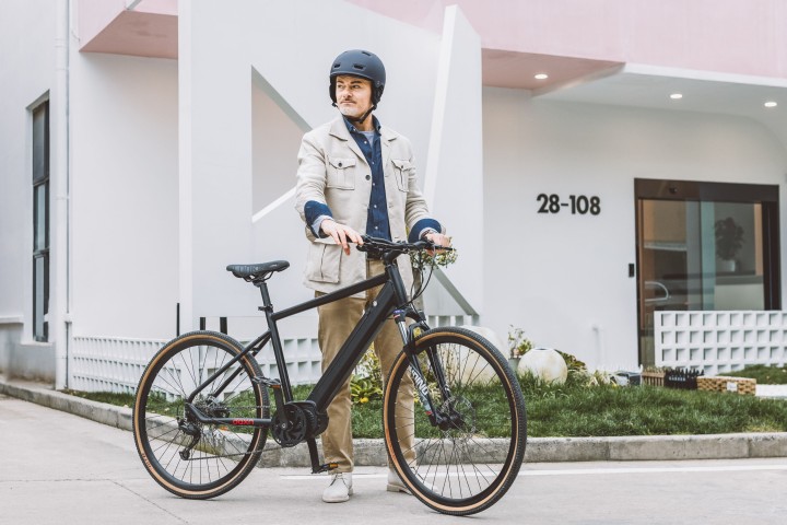 Mann mit helm steht vor seinem Haus neben seinem E-Bike