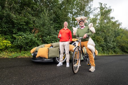 Ralf Schumacher und ein mit Kissen gepolsterter Fahrradfahrer stehen vor einem mit Kissen gepolsterten Auto und halten Daumen hoch.