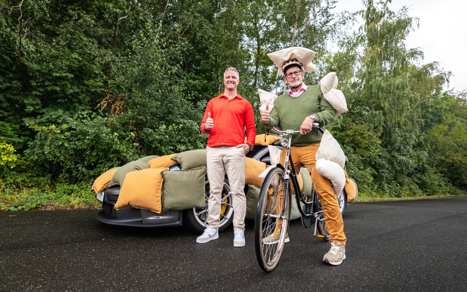 Ralf Schumacher und ein mit Kissen gepolsterter Fahrradfahrer stehen vor einem mit Kissen gepolsterten Auto und halten Daumen hoch.