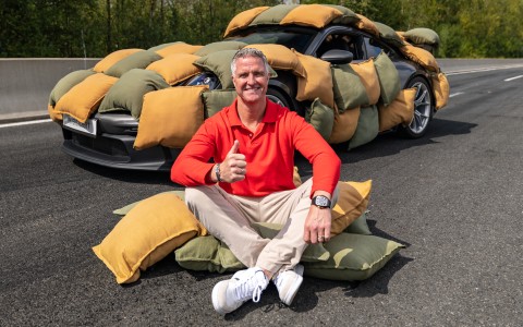 Ralf Schumacher sitzt auf einem Haufen Kissen vor einem mit Kissen ummantelten Auto.