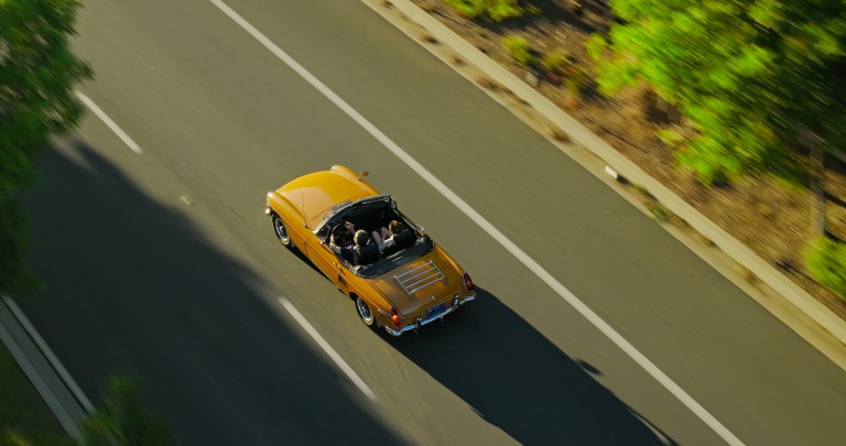 Draufsicht auf ein gelbes Oldtimer-Cabiro, das über eine mit Bäumen gesäumte Kandstrasse fährt