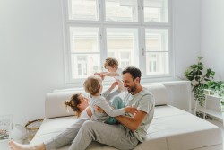 Familie tobt glüklich auf dem Sofa in einm hellen Wohzimmer