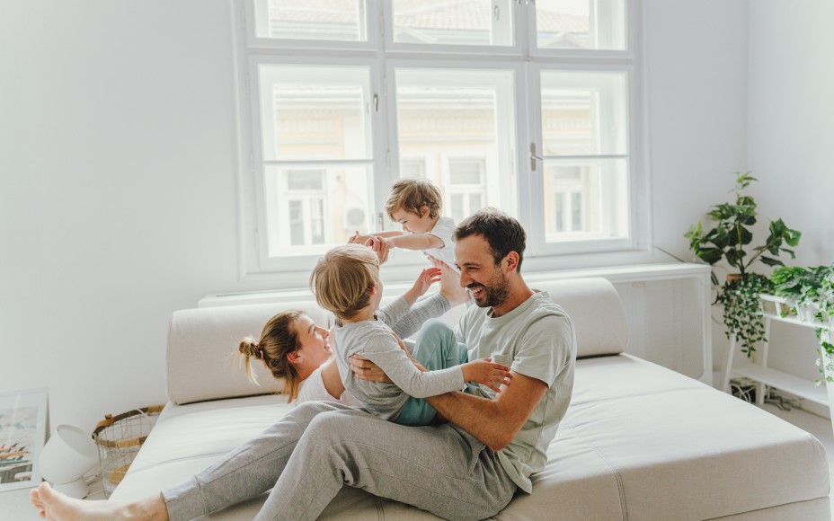 Familie tobt glüklich auf dem Sofa in einm hellen Wohzimmer