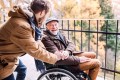 Ein junger Mann und ein älterer Mann im Rollstuhl sind zusammen im Freien unterwegs