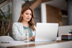 Frau sitzt lächelnd am Schreibtisch vor Laptop
