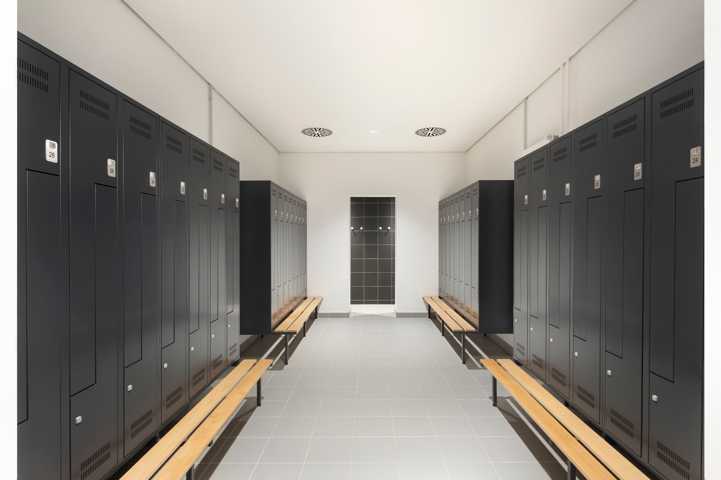 Moderner Umkleideraum mit uni-schwarzen Schränken und hellen Holzbänken