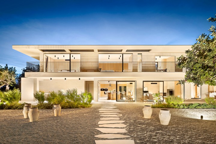 Modernes zweistöckiges Haus bei Abendbeleuchtung, mit großen Glasfronten, Balkon im Obergeschoss, Gartenpflanzen und Steinweg im Vordergrund