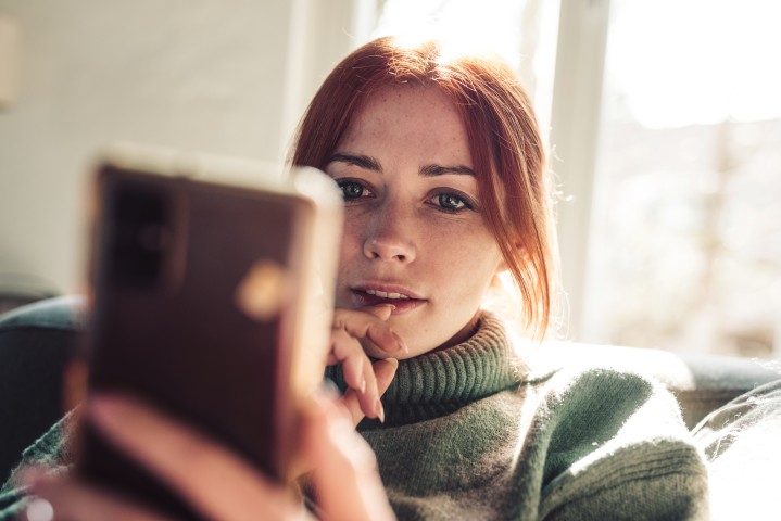 Rothaarige Frau gibt per Smartphone digitales Kundenfeedback oder Online-Bewertung zu einem Versicherungsservice ab und wirkt nachdenklich.