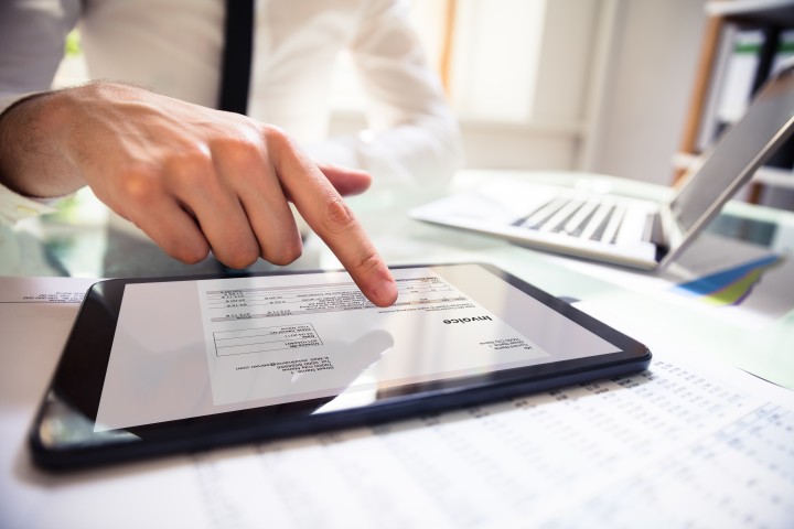 Mann fährt mit dem Zeigefinger über ein Tablet, auf dem man Daten und Diagramme sieht